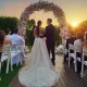 Bride and groom standing under a floral arch at an intimate micro weddings ceremony at sunset.